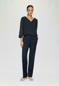 Navy Bluse mit durchsichtigen 3/4-Ärmeln, V-Ausschnitt, kombiniert mit maßgeschneiderten navyfarbigen gemusterten Hosen und offenen Sandalen. Minimalistisches Design.