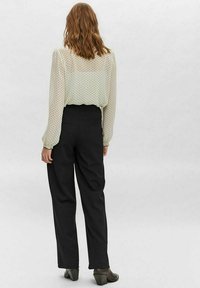 Blusa a pois verde chiaro abbinata a pantaloni neri a vita alta, entrambi di vestibilità rilassata. La blusa presenta maniche lunghe e una texture traslucida.