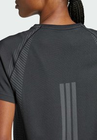 Primo piano di una persona che indossa una maglietta sportiva grigio scuro con tre strisce riflettenti verticali sulla parte superiore della schiena e capelli intrecciati raccolti.