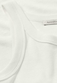 Weißes geripptes Tanktop mit rundem Ausschnitt, weichem Material und einem kleinen Etikett mit "hessnatur" an der Seite.