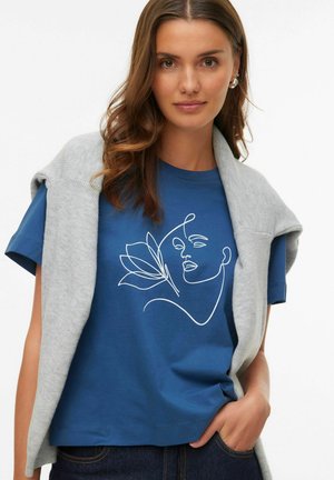 Blue cotton t-shirt featuring a white line drawing of a face and flower. Accompanied by a light gray knit sweater draped over the shoulders.