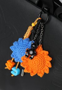 Zwarte tas met kleurrijke gehaakte bloemdecoraties in blauw en oranje, met een zwarte berenaccent en gekleurde kralen bevestigd aan kettingen.