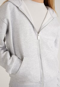 Grijze rits-hoodie gemaakt van zachte stof, met een contrasterende binnenvoering, zijzakken en ribgebreide boorden en zoom.
