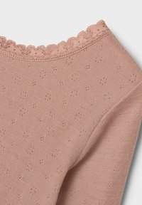 Haut tricoté rose clair avec un col en dentelle festonné, présentant un motif texturé avec de petits designs floraux répartis sur le tissu.
