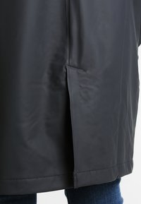 Czarna wodoodporna kurtka o gładkiej fakturze, z boczną kieszenią i prostym dołem. Brak widocznych wzorów lub ozdobnych elementów.