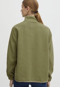 Giacca in pile verde oliva con collo alto, polsini elastici e superficie testurizzata. Presenta un taglio dritto e una vestibilità casual.