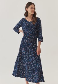 Robe marine à manches trois-quarts, ornée d'un motif de feuilles roses et bleues dispersées, avec un corsage ajusté et une jupe évasée en dessous du genou.