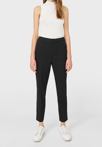 Zwarte gestreepte broeken met een getailleerde pasvorm, gemaakt van een gladde stof, gecombineerd met een witte mouwloze top en witte sneakers.