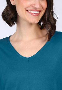 Türkises V-Neck-Top aus weichem, glattem Stoff mit lockerer Passform und leichtem Glanz; verfügt über eine dezente Nahtdetails am Ausschnitt.