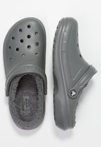 Zoccoli grigi Crocs con fori di ventilazione, interno morbido e strap posteriore. Suola in gomma texturizzata e dettagli di branding discreti.