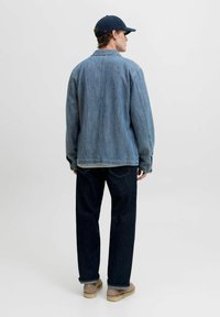 Veste en denim bleu clair avec une coupe décontractée, des manches longues et des détails en boutons, associée à un jean bleu foncé et des chaussures beige.