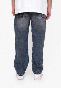 Jeans in denim con vestibilità ampia, colore blu scuro sbiadito, polsini elastici e due tasche posteriori con dettagli di cucitura discreti.