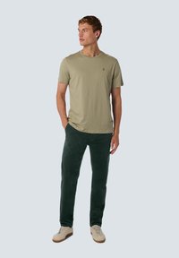 Licht olijfgroene t-shirt met een ronde hals, gecombineerd met donkergroene corduroy broek. Lichtbeige sneakers maken de outfit compleet.