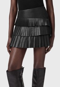 Μαύρη πλισέ μίνι φούστα από δέρμα, με λείο λάστιχο στη μέση και στρώματα υφής με κάθετες πτυχές για λεπτομέρεια και κίνηση.