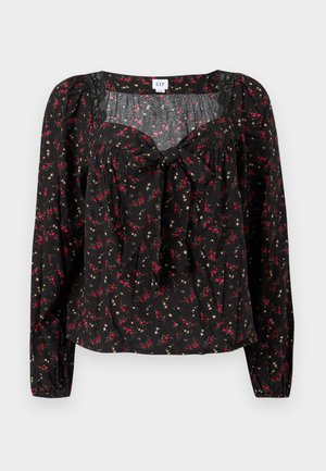 Sort blomstret bluse med lange ærmer, der har bindebånd foran, rynkede detaljer og små røde og hvide blomsterprint over det hele.