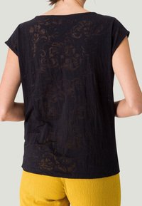 Top corto nero a maniche corte con un motivo floreale testurizzato. Il tessuto è leggero e semi-trasparente, con una vestibilità rilassata.