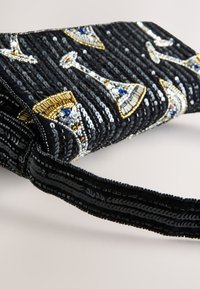 Pochette noire ornée de perles avec des paillettes et des accents métalliques en or et argent. Détail avec un motif décoratif de flûte à champagne.