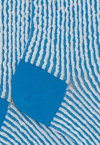 Calze a righe blu e bianche con un motivo a maglia testurizzata e tallone blu unito. Linee ondulate creano un effetto visivo distintivo.