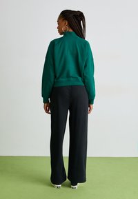 Grön sweatshirt med hög krage och sänkta axlar, tillsammans med svarta vida byxor. Tyget ser mjukt ut med en avslappnad passform.
