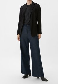Sort blazer over en mørk bluse, parret med brede mørke denim jeans. Sorte hælankelstøvler fuldender outfittet.