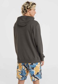 Donkergrijze hoodie met een losse pasvorm, gecombineerd met een korte broek met bloemenpatroon in blauw, geel en zwart.