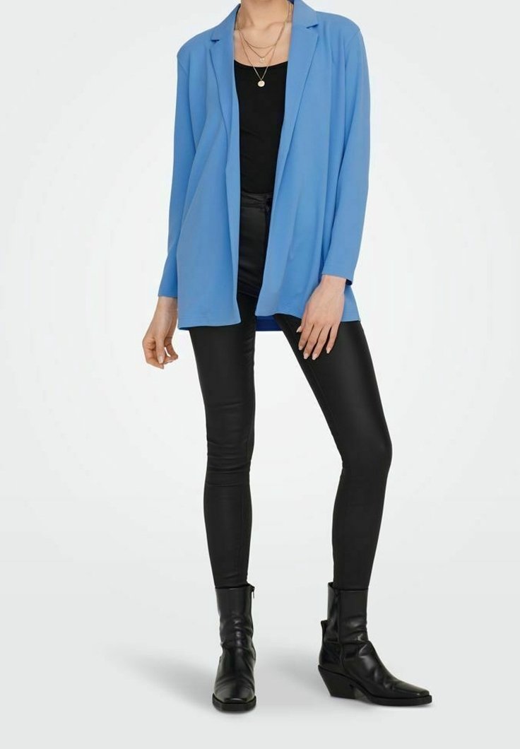Blazer de tela suave en azul claro, de corte holgado, con solapas muestradas, combinado con pantalones negros ajustados y botas de tobillo. Diseño minimalista.
