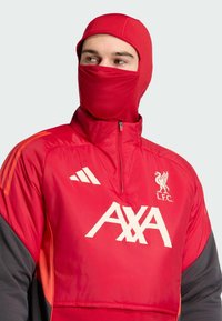 Red athletic jacket with a high collar, featuring white logo details and orange accents. The fabric appears smooth and slightly shiny.