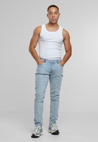Világoskék, slim fit farmernadrág, öt zsebes kialakítással és diszkrét varrással. Fehér ujjatlan top és szürke sportcipő társításával.
