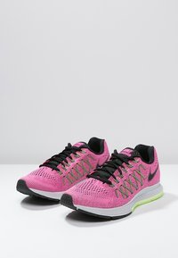 Un paio di scarpe da corsa Nike rosa con loghi swoosh neri, lacci neri, intersuole bianche e dettagli verde neon sulle suole.