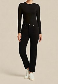 Top negro de manga larga combinado con jeans negros de pierna recta. Zapatillas blancas completan el look. Tela suave con un diseño ceñido.