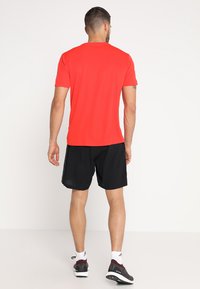 Camiseta deportiva roja de manga corta con cuello redondo, combinada con pantalones cortos negros. El conjunto cuenta con una tela transpirable y un diseño de corte relajado.
