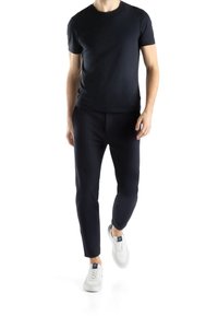 Schwarzes T-Shirt mit kurzen Ärmeln, kombiniert mit dunklen Hosen. Beide Kleidungsstücke bestehen aus glattem Stoff. Abgerundet mit weißen Sneakern.