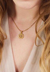 Gouden ketting met een ronde hanger waarop een hoofdletter "R" staat, met een delicate ketting. Glad afgewerkt, minimalistisch ontwerp.