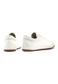 Białe skórzane sneakersy mają niskoprofilowy design, okrągły czubek i subtelne faktury. Podeszwa jest w jasnobrązowym kolorze, kontrastującym z cholewką.