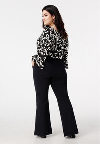 Zwart-wit top met patroon en klokkende mouwen, gecombineerd met zwarte uitlopende broek. Het ontwerp bevat krullen en heeft een gladde textuur.