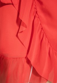 Vestido coral con volantes y tejido texturizado, con volantes en capas a lo largo del lado y un dobladillo semitransparente para mayor detalle y dimensión.