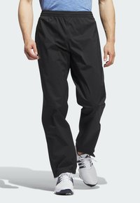 Pantalons noirs, légers et imperméables avec une taille élastique et une coupe décontractée, dotés de poches latérales et d'une texture lisse.