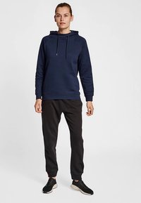 Granatowa bluza z kapturem ze sznurkiem, długimi rękawami i ściągaczami na mankietach. Do tego czarne spodnie dresowe i czarne buty sportowe.