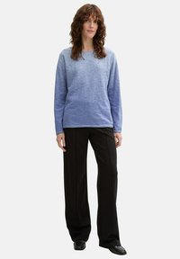 Hellblau strukturierter Pullover mit langen Ärmeln, kombiniert mit schwarzen weit geschnittenen Hosen. Einfaches Design, minimale Akzente.