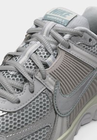 Artimos plano pilkos spalvos Nike Vomero 5 sportinio batelio sugedusi medžiaga, raišteliai, gofruotas šoninis skydelis ir Nike logotipas.
