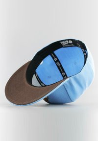 Sininen lippalakki ruskealla lippaalla, teksturoitu kangas, istuva muotoilu ja sisäpuolella koko- ja bränditiedot. Lippalakin alareuna on täysin sininen.