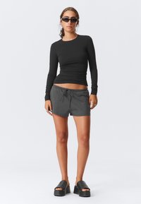 Cămașă neagră cu mâneci lungi, pantaloni scurți gri cu șnur, și sandale cu platformă neagră masive. Model purtând ochelari de soare și un inel de argint.