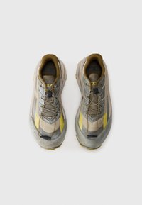 Baskets de sport gris clair et beige avec des accents jaunes, en matériau synthétique et en maille, tige texturée et lacets élastiques.