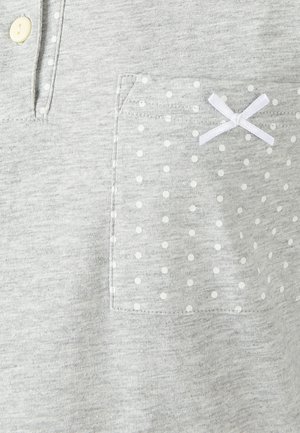 Camisa de algodón gris con tapeta de botones, que presenta un bolsillo con lunares y un detalle de lazo blanco. Textura suave y diseño casual.