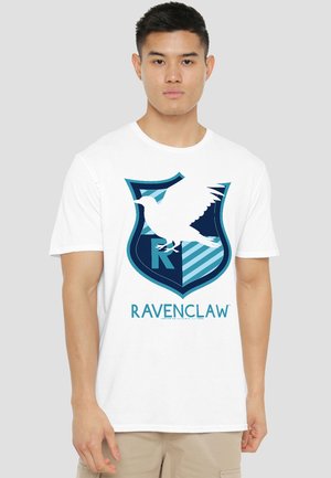 Young man wearing a white t-shirt with a blue Ravenclaw crest featuring a bird and the word "Ravenclaw" on a plain background.