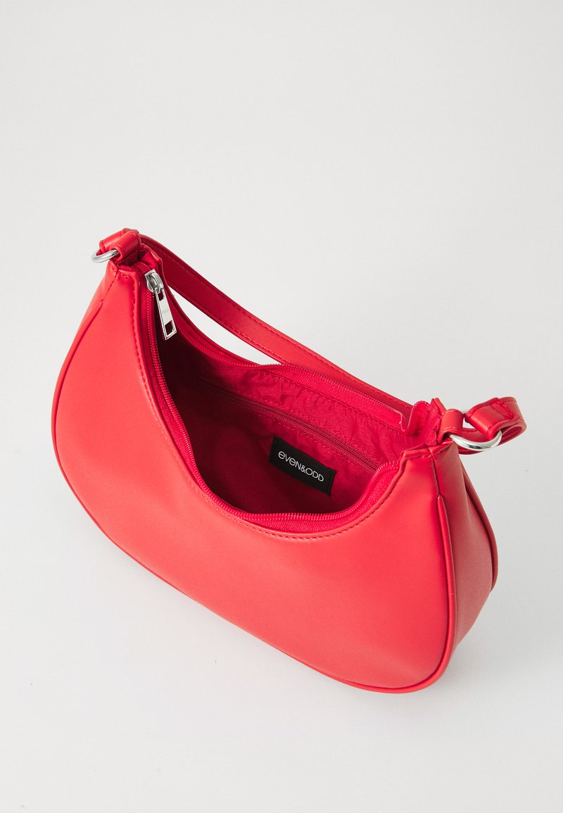 Bolso de mano rojo de cuero sintético con forma curvada, cierre superior con cremallera y una correa corta. El interior cuenta con un forro de tela y un pequeño bolsillo con cremallera.