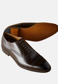 Zapatos de vestir de piel marrón con un acabado suave, diseño de puntera tipo cap toe, detalles de brogue y una suela marrón de contraste. Estilo de cordones.