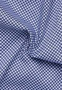 Tessuto di cotone di un blu chiaro con un motivo geometrico di cerchi e quadrati navy. Texture liscia, peso medio, con una leggera lucentezza.