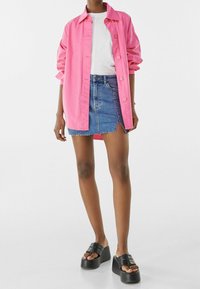 Růžová košilová košile přes bílém tričku, spárovaná s džínovou sukní s odstřiženými okraji a černými platformovými sandály. Jednoduchý, neformální styl.