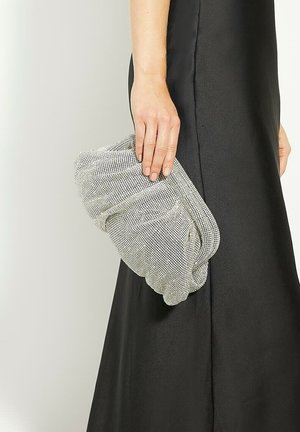 Pochette en maille argentée avec un design drapé, ornée de fils métalliques et d'une forme arrondie, tenue à la main contre une robe en satin noir.